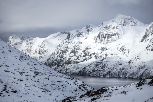 View of snow covered mountain peaks overlooking the calm waters of a fjord under a cloudy winter sky in Ersfjord Troms Norway. View of snow covered mountain peaks overlooking the calm waters of a fjord under a cloudy winter sky in Ersfjord Troms Norway.