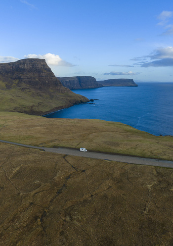 Aerial view of a white campervan driving along a coastal road near the rugged cliffs of Neist Point Isle of Skye Scotland United Kingdom. Aerial view of a white campervan driving along a coastal road near the rugged cliffs of Neist Point Isle of Skye Scotland United Kingdom.