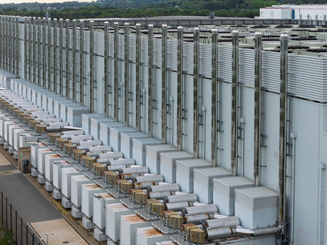 Aerial view of a large data center facility featuring rows of industrial cooling units and ventilation pipes along the exterior wall of a modern building United Kingdom.