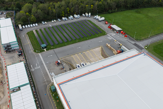 Aerial view of a data center facility featuring a large solar panel array a parking lot with white vans and a warehouse building in the United Kingdom.