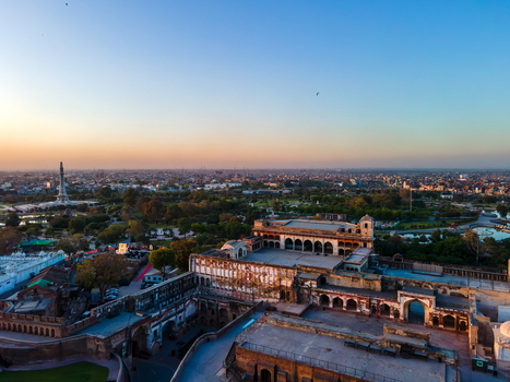 Aerial view of Lahore Fort featuring historic Mughal architecture expansive courtyards and surrounding lush gardens under a clear sunset sky in Lahore Punjab Pakistan.