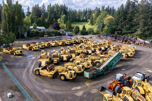 Woodburn Oregon United States 25 September 2026 Aerial view of a large collection of yellow construction machinery including scrapers and loaders parked in a gravel lot surrounded by trees. Woodburn Oregon United States 25 September 2026 Aerial view of a large collection of yellow construction machinery including scrapers and loaders parked in a gravel lot surrounded by trees.