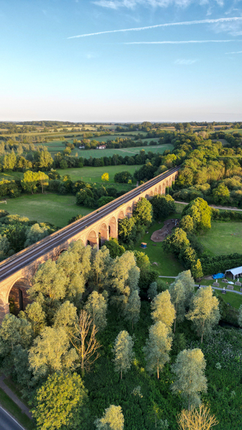 Aerial view of Chappel Viaduct spanning across the lush green landscape with trees and fields in Chappel England United Kingdom.