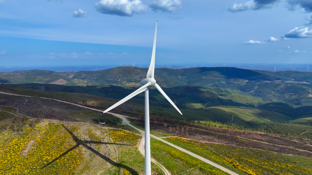 Aerial view of a wind turbine standing on a grassy hill covered in yellow flowers with rolling hills and a clear blue sky in the background in Lisbon Lisbon Portugal. Aerial view of a wind turbine standing on a grassy hill covered in yellow flowers with rolling hills and a clear blue sky in the background in Lisbon Lisbon Portugal.