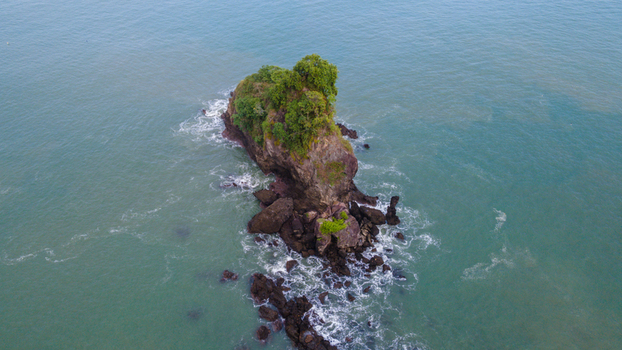 Aerial view of the iconic rocky outcrop of Karang Agung Beach covered in lush green trees surrounded by turquoise ocean waves Ayah Central Java Indonesia. Aerial view of the iconic rocky outcrop of Karang Agung Beach covered in lush green trees surrounded by turquoise ocean waves Ayah Central Java Indonesia.