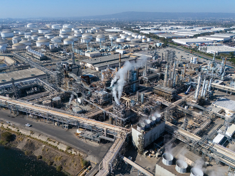 Aerial view of an industrial oil refinery with numerous storage tanks complex piping systems and smoking chimneys in Carson California United States.