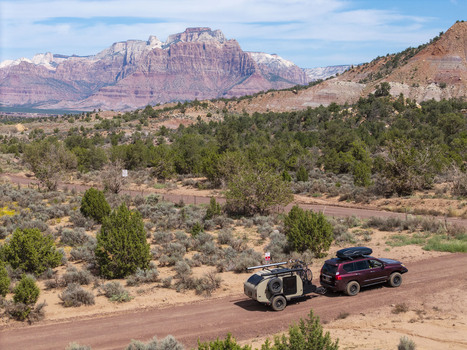 Aerial view of an SUV pulling a teardrop camper trailer on a dirt road at Gooseberry Mesa with Zion National Park mountains in the background in Hurricane Utah United States. Aerial view of an SUV pulling a teardrop camper trailer on a dirt road at Gooseberry Mesa with Zion National Park mountains in the background in Hurricane Utah United States.