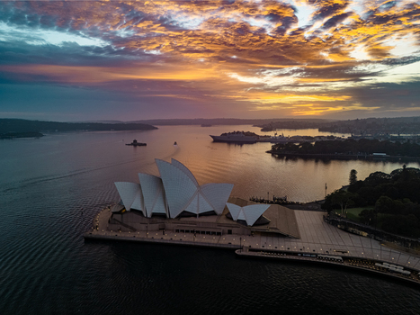 Aerial view of the iconic Sydney Opera House silhouetted against a fiery dawn sky reflecting on the tranquil harbor waters Sydney New South Wales Australia. Aerial view of the iconic Sydney Opera House silhouetted against a fiery dawn sky reflecting on the tranquil harbor waters Sydney New South Wales Australia.