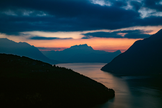 Aerial view of the Swiss Alps at sunset with dark mountain silhouettes reflected in the calm lake waters under a vibrant orange and purple sky in Airolo Ticino Switzerland. Aerial view of the Swiss Alps at sunset with dark mountain silhouettes reflected in the calm lake waters under a vibrant orange and purple sky in Airolo Ticino Switzerland.
