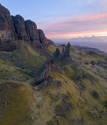 Aerial view of The Storr rock formations with the Old Man of Storr pinnacle under a pink sunset sky on the Trotternish peninsula Isle of Skye Scotland United Kingdom. Aerial view of The Storr rock formations with the Old Man of Storr pinnacle under a pink sunset sky on the Trotternish peninsula Isle of Skye Scotland United Kingdom.