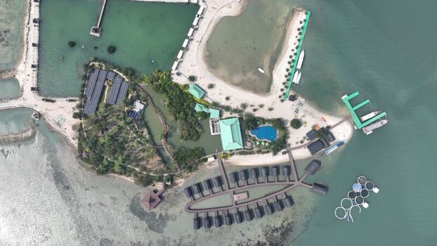 Aerial view of Pulau Lima Resort featuring overwater bungalows a swimming pool and lush greenery surrounded by clear coastal waters in Kasemen Banten Indonesia. Aerial view of Pulau Lima Resort featuring overwater bungalows a swimming pool and lush greenery surrounded by clear coastal waters in Kasemen Banten Indonesia.