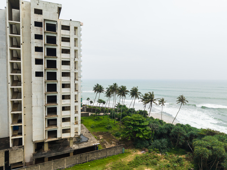 Aerial view of an unfinished high rise building standing near a tropical coastline with palm trees and ocean waves in Galle Southern Province Sri Lanka. Aerial view of an unfinished high rise building standing near a tropical coastline with palm trees and ocean waves in Galle Southern Province Sri Lanka.