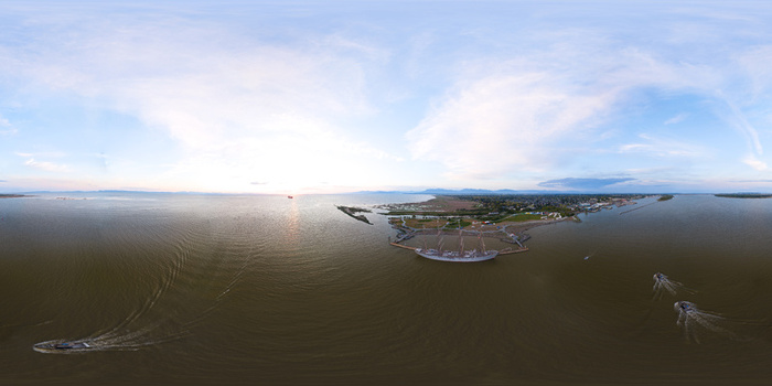 Aerial view of a large sailing ship docked at a pier with small boats navigating the calm coastal waters during a golden sunset in Metro Vancouver A British Columbia Canada.