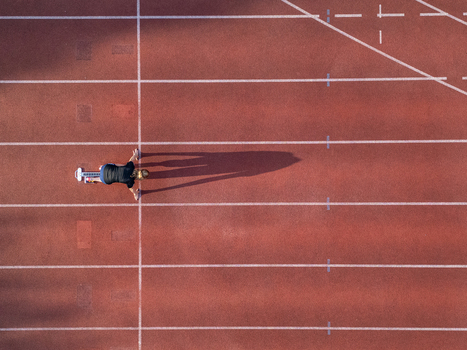 Aerial view of a female athlete in starting blocks on a red running track with white lane markings and long shadows in Almere Flevoland Netherlands.