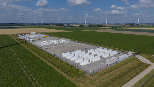 Aerial view of a battery energy storage system with white containers in a fenced compound surrounded by agricultural fields and wind turbines in Dronten Flevoland Netherlands. Aerial view of a battery energy storage system with white containers in a fenced compound surrounded by agricultural fields and wind turbines in Dronten Flevoland Netherlands.