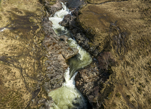 Aerial view of Glen Etive Waterfall with rushing water flowing through a rocky gorge and brown moorland in Ballachulish Scotland United Kingdom.