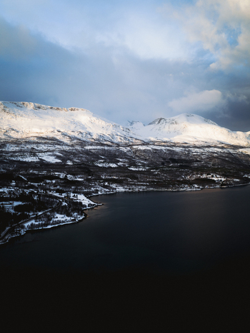 Aerial view of snow dusted mountains meeting the dark waters under a cloudy sky a stark contrast of nature s elements Sjøvegan Troms Norway. Aerial view of snow dusted mountains meeting the dark waters under a cloudy sky a stark contrast of nature s elements Sjøvegan Troms Norway.
