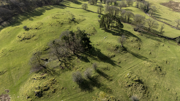 Aerial view of rolling green hills dotted with clumps of trees casting long shadows under a bright sky Ambleside England United Kingdom. Aerial view of rolling green hills dotted with clumps of trees casting long shadows under a bright sky Ambleside England United Kingdom.