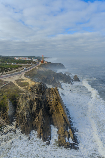 Aerial view of Farol Penedo da Saudade on rugged cliffs with crashing waves and a coastal road in Marinha Grande Leiria Portugal. Aerial view of Farol Penedo da Saudade on rugged cliffs with crashing waves and a coastal road in Marinha Grande Leiria Portugal.