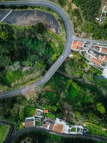Aerial view of a winding road cutting through vibrant green forests and quaint buildings showcasing the contrast between nature and architecture Agua de Alto Azores Portugal.