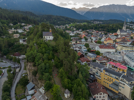 Aerial view of St. Laurentius Church perched on a hill overlooking the alpine town of Imst with surrounding mountains and lush greenery in Imst Tyrol Austria.