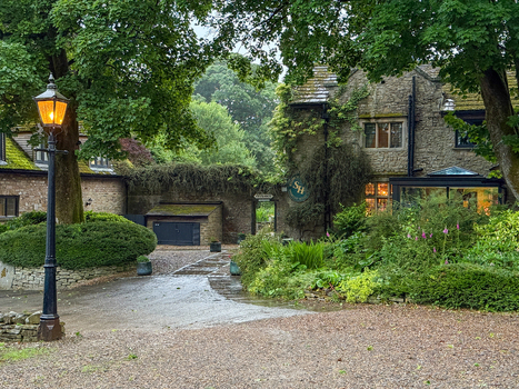 View of a historic stone building with a lit vintage street lamp and lush green gardens in Hawes England United Kingdom. View of a historic stone building with a lit vintage street lamp and lush green gardens in Hawes England United Kingdom.