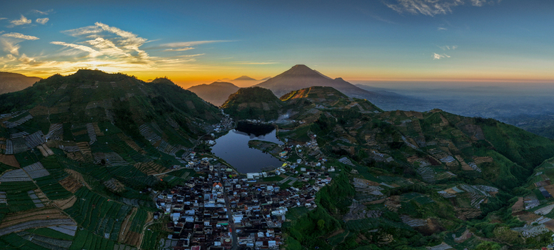 Aerial view of the village of Sikunang and Telaga Cebong lake surrounded by terraced fields and mountains at sunrise in Kecamatan Kejajar Jawa Tengah Indonesia.