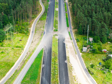 Aerial view of the Southern Bridge project construction site featuring new asphalt roads and infrastructure surrounded by lush green forests in Riga Latvia. Aerial view of the Southern Bridge project construction site featuring new asphalt roads and infrastructure surrounded by lush green forests in Riga Latvia.
