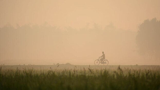 View of a person riding a bicycle through thick fog Bangladesh. View of a person riding a bicycle through thick fog Bangladesh.