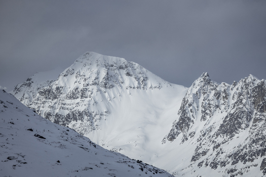 View of snow covered mountain peaks and rugged ridges under an overcast grey sky in Ersfjord Troms Norway. View of snow covered mountain peaks and rugged ridges under an overcast grey sky in Ersfjord Troms Norway.