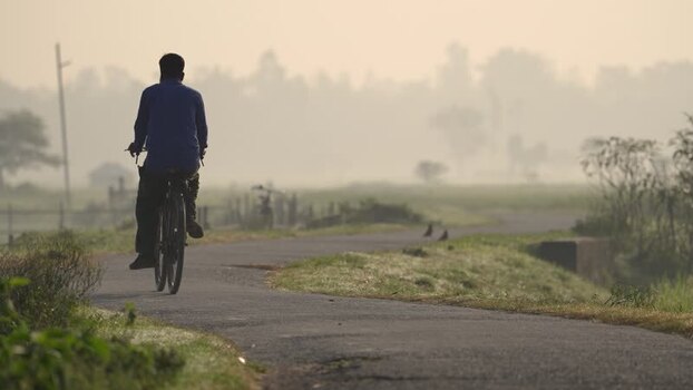 View of a man riding a bicycle on a misty rural road Bangladesh.