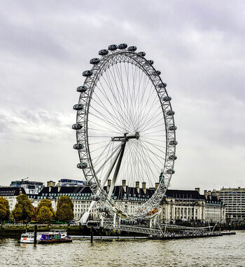 View of the London Eye observation wheel on the South Bank of the River Thames with historic buildings and autumn trees in the background in London United Kingdom.