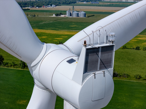 Aerial view of a wind turbine hub with blades and sensors set against a backdrop of agricultural fields and grain silos in Lakeshore Ontario Canada. Aerial view of a wind turbine hub with blades and sensors set against a backdrop of agricultural fields and grain silos in Lakeshore Ontario Canada.