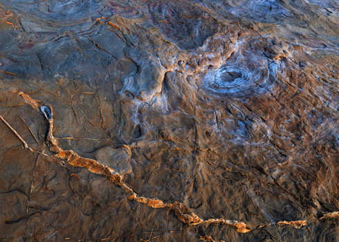 View of the intricate geological textures and swirling patterns of the coastal rocks at Calafuria showing deep cracks salt deposits and warm mineral tones Calafuria Toscana Italy.