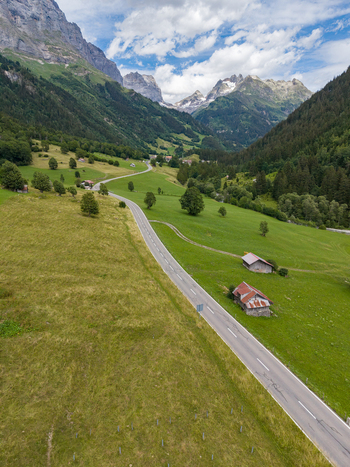 Aerial view of a winding mountain road cutting through lush green meadows and alpine pastures in Gadmen Switzerland.