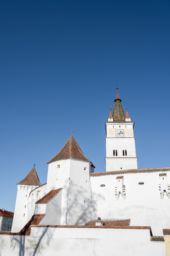 View of the Prejmer Fortified Church with its white walls red tiled roofs and clock tower under a clear blue sky in Prejmer Brasov Romania. View of the Prejmer Fortified Church with its white walls red tiled roofs and clock tower under a clear blue sky in Prejmer Brasov Romania.