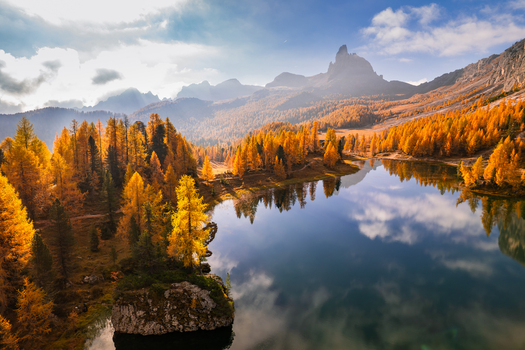 Aerial view of Lago Federa surrounded by vibrant golden larch trees reflecting in the calm lake water and dramatic blue sky in Dolomites Cortina d Ampezzo Veneto Italy. Aerial view of Lago Federa surrounded by vibrant golden larch trees reflecting in the calm lake water and dramatic blue sky in Dolomites Cortina d Ampezzo Veneto Italy.