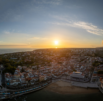Aerial view of the coastal town of Cascais at sunset with red tiled rooftops sandy beaches and the sun reflecting on the Atlantic Ocean in Cascais Lisbon Portugal.