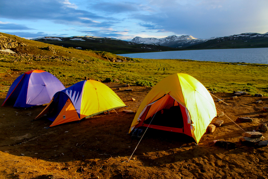 View of colorful camping tents pitched on the grassy shore of Sheosar Lake with snow capped mountains in the background in Skardu Pakistan. View of colorful camping tents pitched on the grassy shore of Sheosar Lake with snow capped mountains in the background in Skardu Pakistan.