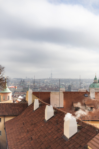 View of historic red tiled rooftops with smoking chimneys overlooking the cityscape under a cloudy sky Prague Prague Czechia. View of historic red tiled rooftops with smoking chimneys overlooking the cityscape under a cloudy sky Prague Prague Czechia.