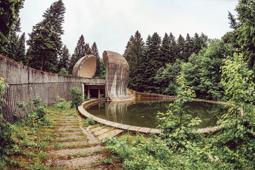 View of the brutalist Korcanica Memorial Zone monument with curved concrete walls and a reflection pool in Sanski Most Federation of Bosnia Bosnia and Herzegovina. View of the brutalist Korcanica Memorial Zone monument with curved concrete walls and a reflection pool in Sanski Most Federation of Bosnia Bosnia and Herzegovina.