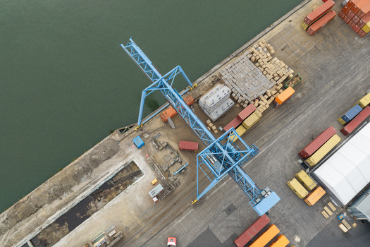Aerial view of the Haven Genk inland port featuring a large blue gantry crane stacks of shipping containers and cargo logistics infrastructure along the industrial waterfront in Genk Vlaanderen Belgium.