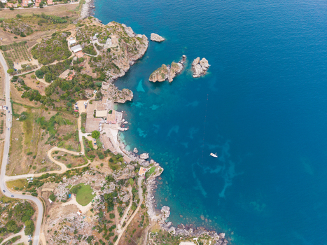 Aerial view of the rugged coastline of Sicily with turquoise waters rocky cliffs a small beach and a winding road along the shore in Palermo Sicily Italy. Aerial view of the rugged coastline of Sicily with turquoise waters rocky cliffs a small beach and a winding road along the shore in Palermo Sicily Italy.