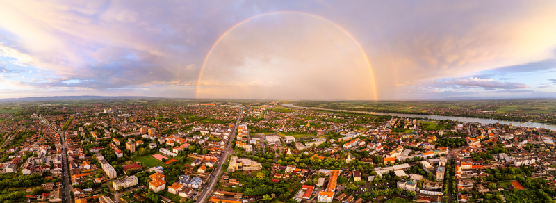 Aerial view of a vibrant double rainbow arching over the city rooftops and the Sava River during sunset in Sremska Mitrovica Serbia.
