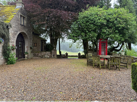 View of a traditional stone cottage with a gravel courtyard wooden furniture and a red telephone box overlooking the rolling hills of Yorkshire in Hawes England United Kingdom. View of a traditional stone cottage with a gravel courtyard wooden furniture and a red telephone box overlooking the rolling hills of Yorkshire in Hawes England United Kingdom.