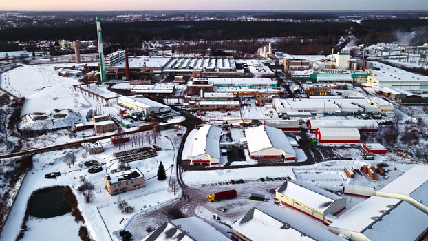 Aerial view of an industrial complex with snow covered factory buildings tall chimneys and a truck parked on the grounds during winter in Latvia. Aerial view of an industrial complex with snow covered factory buildings tall chimneys and a truck parked on the grounds during winter in Latvia.