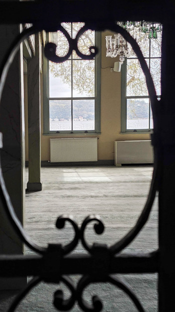 View of the interior of a historic building with ornate chandeliers and large windows overlooking the Bosphorus through a decorative iron gate Sariyer Istanbul Turkiye.
