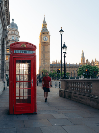 View of an iconic crimson telephone booth contrasting with a lone figure strolling past the towering golden hued Big Ben under a serene sky London England United Kingdom. View of an iconic crimson telephone booth contrasting with a lone figure strolling past the towering golden hued Big Ben under a serene sky London England United Kingdom.