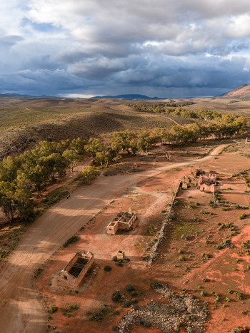 Aerial view of the historic Kanyaka Station ruins and a winding dirt road surrounded by arid landscape and trees under a cloudy sky in Flinders Ranges South Australia Australia. Aerial view of the historic Kanyaka Station ruins and a winding dirt road surrounded by arid landscape and trees under a cloudy sky in Flinders Ranges South Australia Australia.