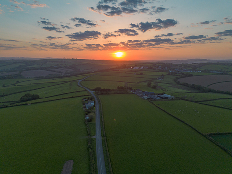 Aerial view of rolling green fields and a winding road at sunset in the countryside Looe Cornwall United Kingdom. Aerial view of rolling green fields and a winding road at sunset in the countryside Looe Cornwall United Kingdom.